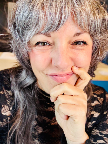 This is a photo of Shannon — a middle-aged woman with grey hair and wearing a lacy black top — holding her chin in her hand and smiling toward the camera.
