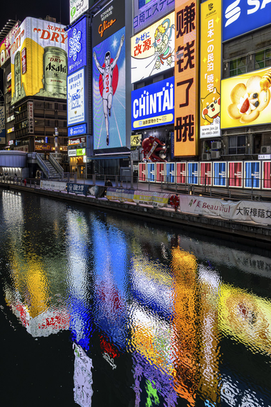 Buildings covered in bright and colourful neon commercials and reflected in the Dotonbori River in Osaka, in Japan at night.