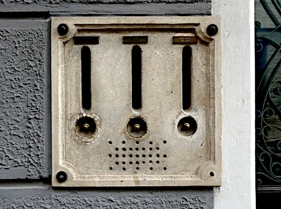 Foto van drie brievenbussen met daaronder belknoppen in stenen plaat aan muur