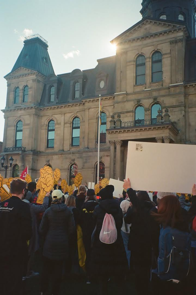 A group of people holding yellow foam fists gathered at the legislature for a CUPE solidarity rally