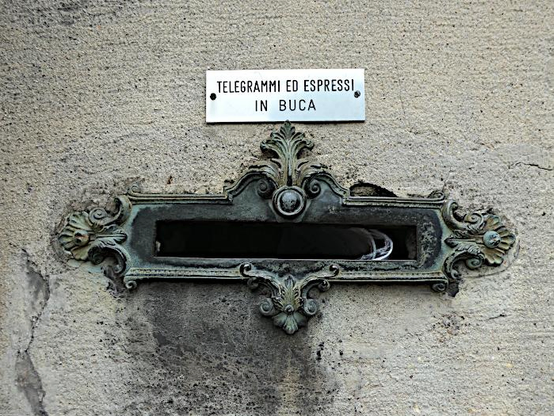 Foto van metalen brievenbus met krullerige ornamenten in muur en klein bordje met tekst: Telegrammen en expressebrieven in het gat