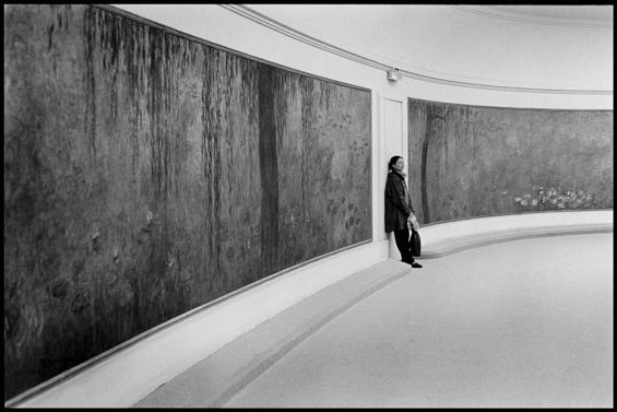 Photo en noir et blanc d'une femme appuyé contre le mur entre 2 immenses toiles des nymphéas de Monet