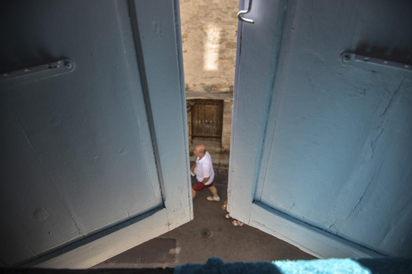 dans l'ouverture entre deux volets mi-clos, un passant en contrebas dans la rue
