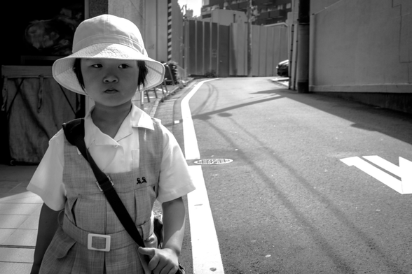 Nena de camí cap a l'escola, amb barret i amb la bossa de travers.