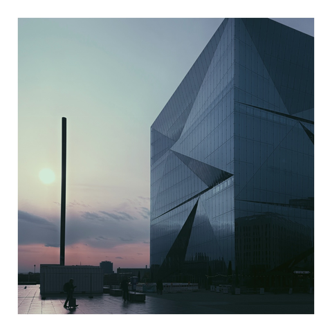 Pastellfarbener Himmel neben einem würfelförmigen Gebäude mit gebrochener Fassade