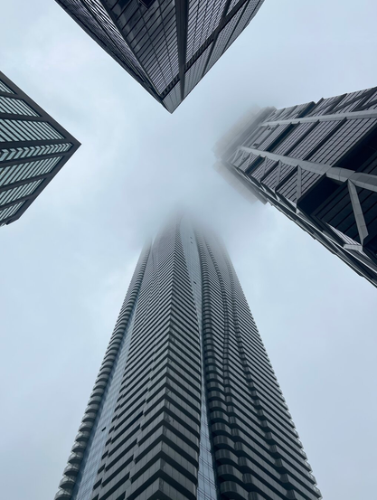 Four grey skyscrapers disappear into a misty foggy sky. Photo was taken straight up.