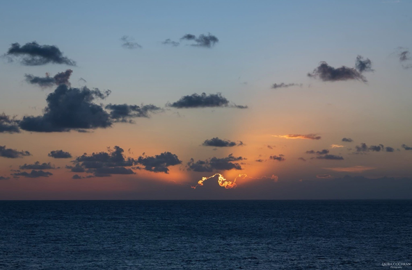 Rays of light from behind clouds during a serene sunset over the sea. 