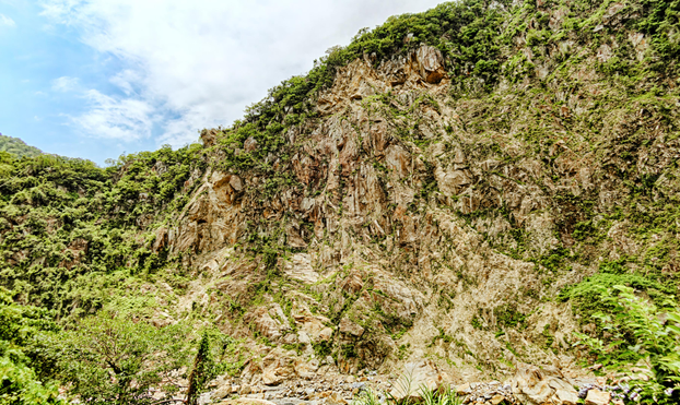 A rocky hill partly covered with shrubs against a cloudy summer sky.