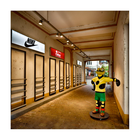 Hausdurchgang zum Hinterhof, auf der linken Seite Leuchtreklame für "Nike" , "Rieker" und "Adidas", auf der rechten Seite die menschhohe Werbefigur von "Salamander"