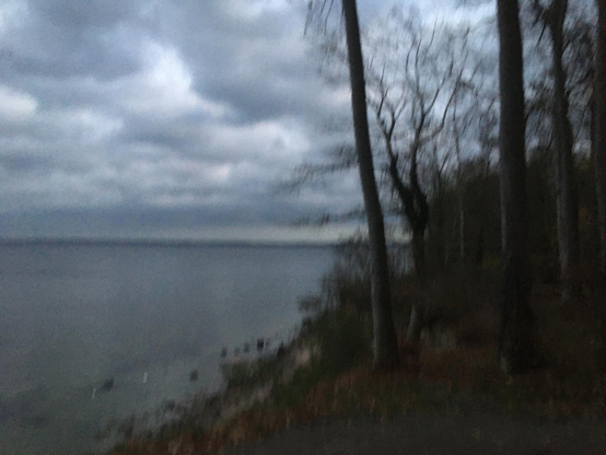 Wolken über der Ostsee. Noch teilweise beleuchtet von der untergegangenen Sonne. Die Ostsee liegt ruhig am Fuße des Steilufers - auf dem im Vordergrund Bäume wachsen. 
Um die abendliche Atmosphäre schnell schwindenden Lichts einzufangen, ist das iPhone SE Foto willentlich verwischt. 