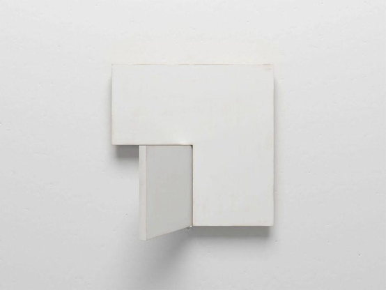 A minimalist white square wall-mounted structure with a small hinged door.