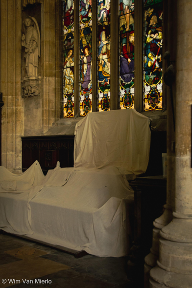Church interior. Underneath the stained-glass window is a side altar that is covered in a white sheet to protect it from dust and grime.