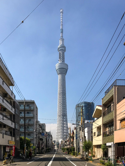 Una avenida de cuatro carriles con edificios de 3-4 alturas a los lados y una torre de comunicaciones enorme al fondo, centrada. Creo que es la construcción de mayor altura de Japón.