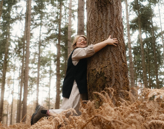 the artist, a young woman ,kneeling in the dry ferns, hugging a tree, smiling