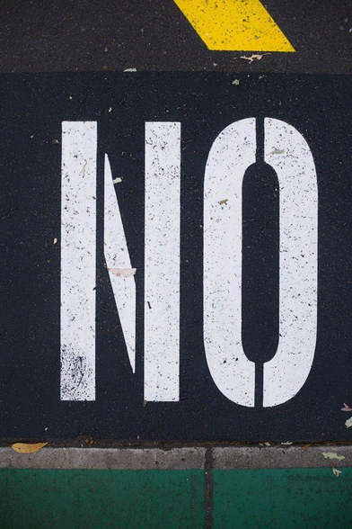 Close-up photo of the white-coloured, all-caps "no" of a "no parking" sign painted on a road.