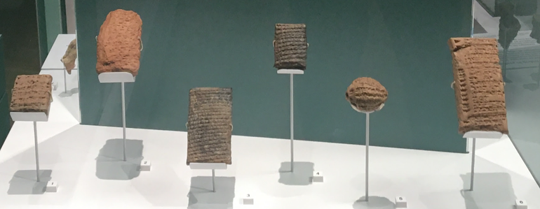 Six stone tablets with cuneiform text on them, mounted on metal stands.