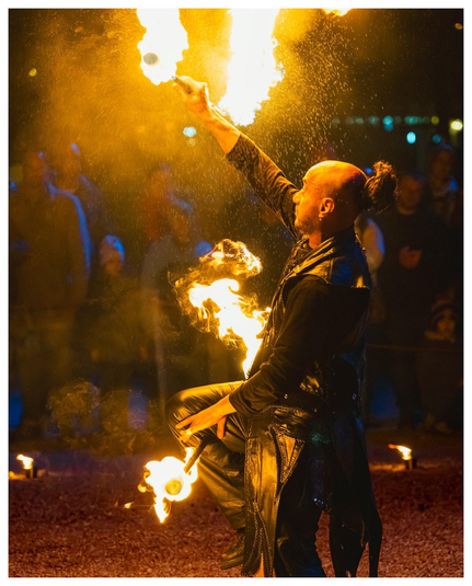 Ein in schwarzes Leder gehüllter Mann jongliert mit brennenden Stangen in der Nacht.