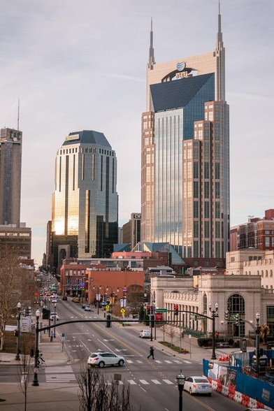 a photo of a large building in the business district of the city, it is light tan with a strip up the center of blue glass, on the left and right sides are points so it sort of looks like an abstract batman head 