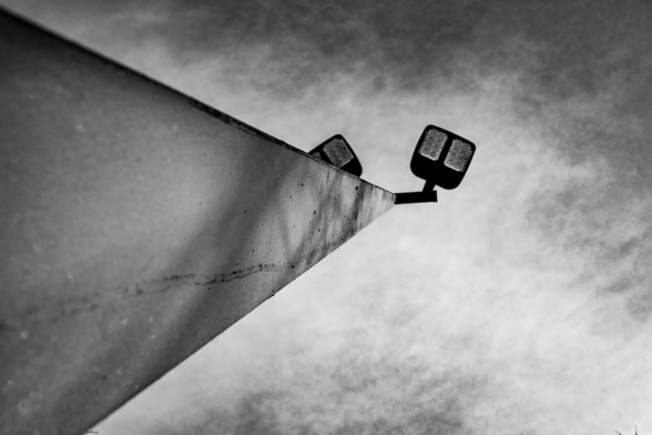 A black and white perspective photo shooting up from a square light post to the lights and sky above.