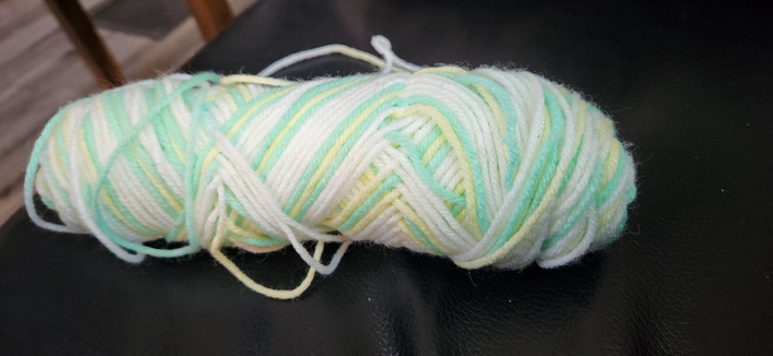 A part skein of pale green, yellow and white variegated yarn. 
