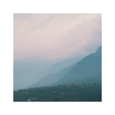 a subtle square image showing the details of a cloudy mountainscape. the sky is hazy after some rain but the early light is already coming through again. the layers of hills become more and more vague towards the distance