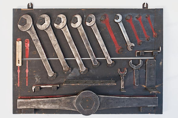 An old board of tools, mostly wrenches, hangs on the wall. Outlines of tools painted in red indicate that some tools have been lost and are missing.