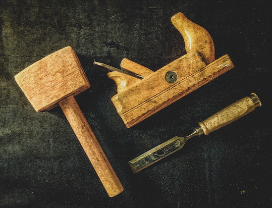 Auf dem Foto sind drei Werkzeuge von einem Schreiner dargestellt. Ein Holzhammer, ein Hobel und ein Stecheisen.