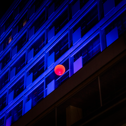Blauw verlichte gevel. Daarvoor is een rode ballon aan een koord zichtbaar.