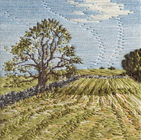 Stitched artwork depicting a hayfield with waving lines of cut hay. A tree to the left casts a shadow across the field