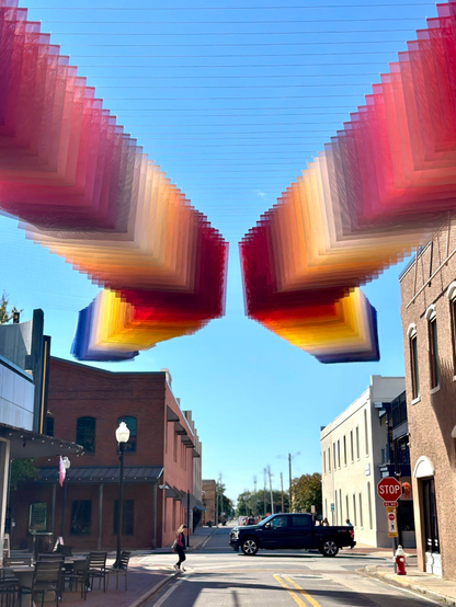 an art installation by Tomislav Topić of layers of colorful planes of fabric suspended above a street, between two buildings, in undulating rows so that it looks prismatic
