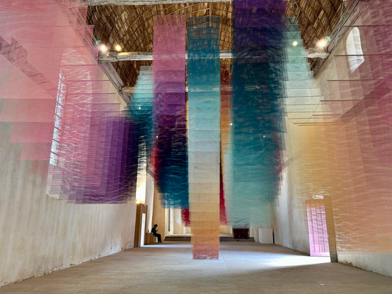 an art installation by Tomislav Topić of layers of colorful planes of fabric suspended from the ceiling in undulating rows so that it looks prismatic
