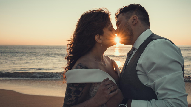Novios se dan un beso en la playa al atardecer.