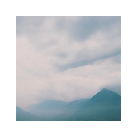 a subtle square image showing the details of a cloudy mountainscape. the sky is hazy after some rain but the early light is already coming through again. the layers of hills become more and more vague towards the distance