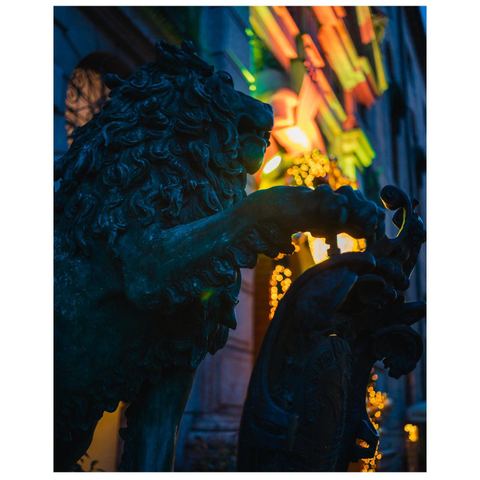 Figur eines Löwen vor einer von kleinen Lampen beleuchteten Gebäudefassade.