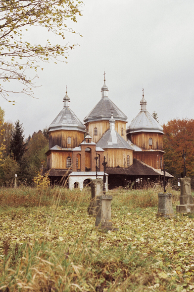 An old brown Orthodox church, visible through dried grass, with branches entering the frame.
