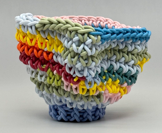 a small, colorful porcelain vessel by Jeremy Brooks that has been made by crocheting long strands of clay
