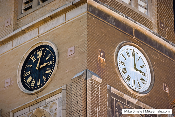 This image shows two clock faces on the corner of a yellow brick church tower. The left half is “normal” with the real colours of yellow bricks, black clock face, and golden Roman numerals with the time showing three minutes past three o’clock. The right side is inverted with the bricks a much darker yellow and the clock face is white with golden Roman numerals. The right side clock is slower and erroneously shows three o’clock.