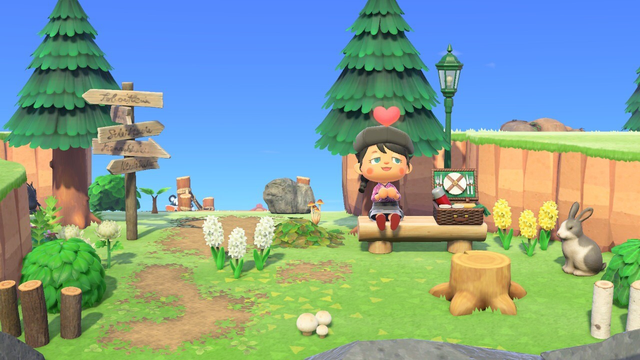 Mein Animal Crossing Charakter sitzt auf einer Bank mit einem Herz-Emoticon über dem Kopf, umgeben von Bäumen, einem Wegweiser, Blumen, einem Picknickkorb und einem Kaninchen in einer farbenfrohen Umgebung.