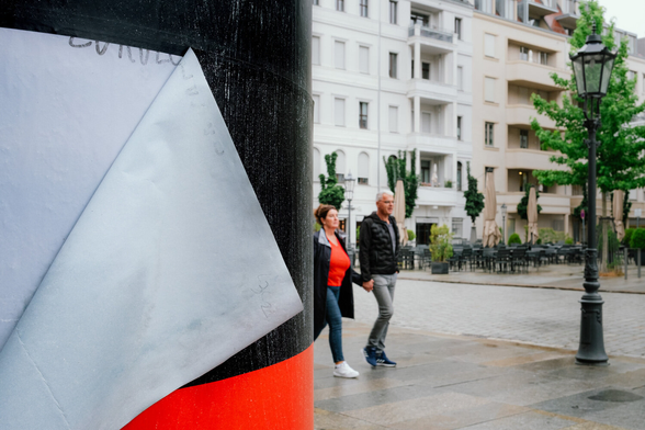 A black-red pillar with a gray triangle. A woman dressed in a red shirt and a black jacket with a gray collar.