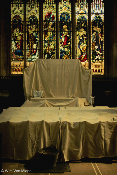 Interior of the church: side altar covered in white sheets to protect it from grime in front of a colourful stained-glass window.