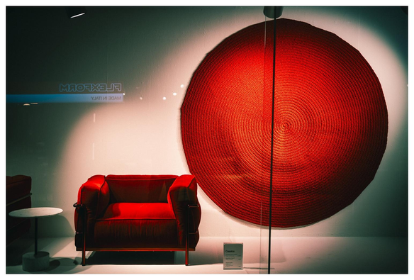 Blick in ein Schaufenster in dem ein roter Sessel und ein runder roter Wandteppich ausgestellt sind.