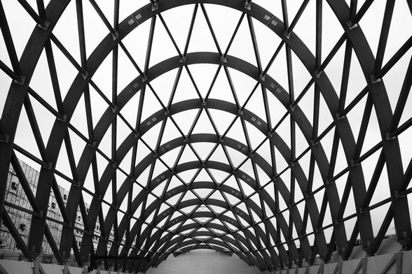 Black-and-white photo of the eel-net inspired design of a road tunnel entryway portal. Thick curved beams create successively shallower archways across the entrance. Thinner beams crisscross these large beams at an angle, creating the effect of a traditional eel net.