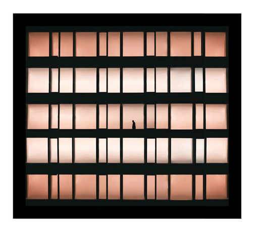 A photo of a rectangular five storey building made of windows with a black frame. The window features a grid of vertical and horizontal black bars. The panes are illuminated in gradient shades of pink and peach. A single small black silhouette of a person, is centered in the middle pane.