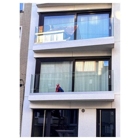 A residential building with multiple balconies. A Spider-Man figure is positioned on the balcony of the second floor, while the ground floor features large glass doors. The building has modern architecture with large windows and light curtains.