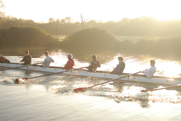 A rowing eight on a river, backlit by the morning sun reflecting off the water