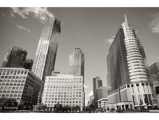 Sepia-toned photo of a modern city skyline with tall, diverse architectural buildings. The scene conveys a sense of urban sophistication and grandeur.
