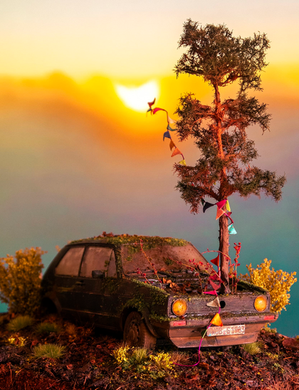 photo of small model car on fake ground looking dirty and rusted next to a tree and a sunset in the background