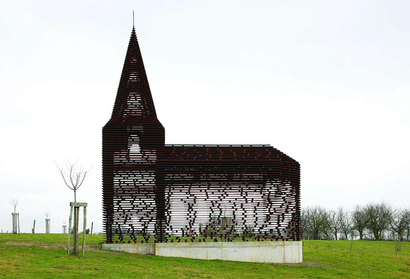 A stylized, see-through wooden church structure with a pointed steeple stands amidst a grassy field under a cloudy sky.