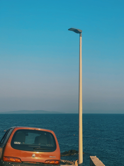 Rotes Auto und ein Laternenmast an am blauen Meer mit blauem Himmel