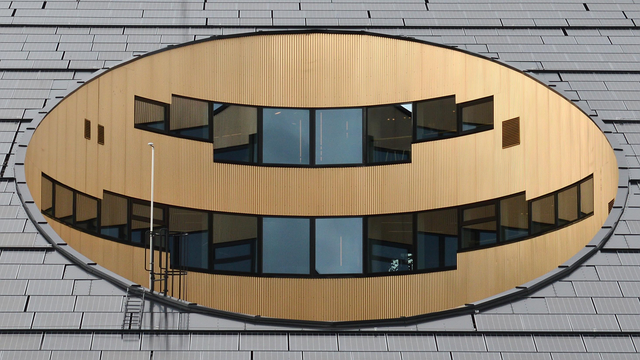 A photo of a golden oval in a grey building with two rows of black windows in it.
